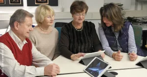 Gruppe Senior:inne sitzt zusammen, schaut auf ein Tablet und lernt den Umgang