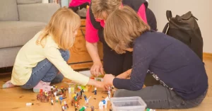 Freiwillige Ilse spielt mit einem blonden Mädchen und einem braunhaarigen Jungen Playmobil